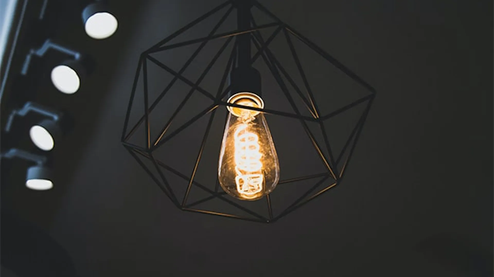 Nowoczesna lampa z drucianym, czarnym abażurem. Wewnątrz dekoracyjna żarówka LED z widoczną spiralą.