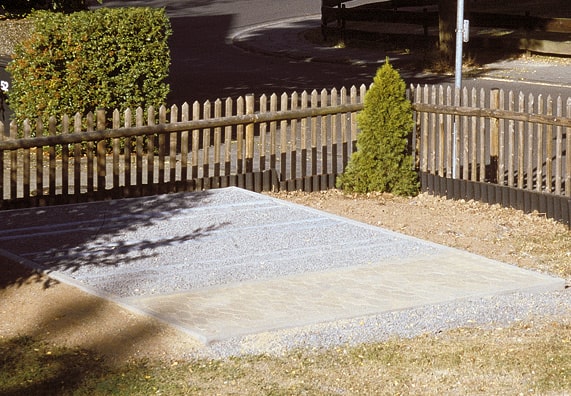 Fundament ciągły z kostki brukowej, obrzeży i kamienia. W tle drewniany płot.