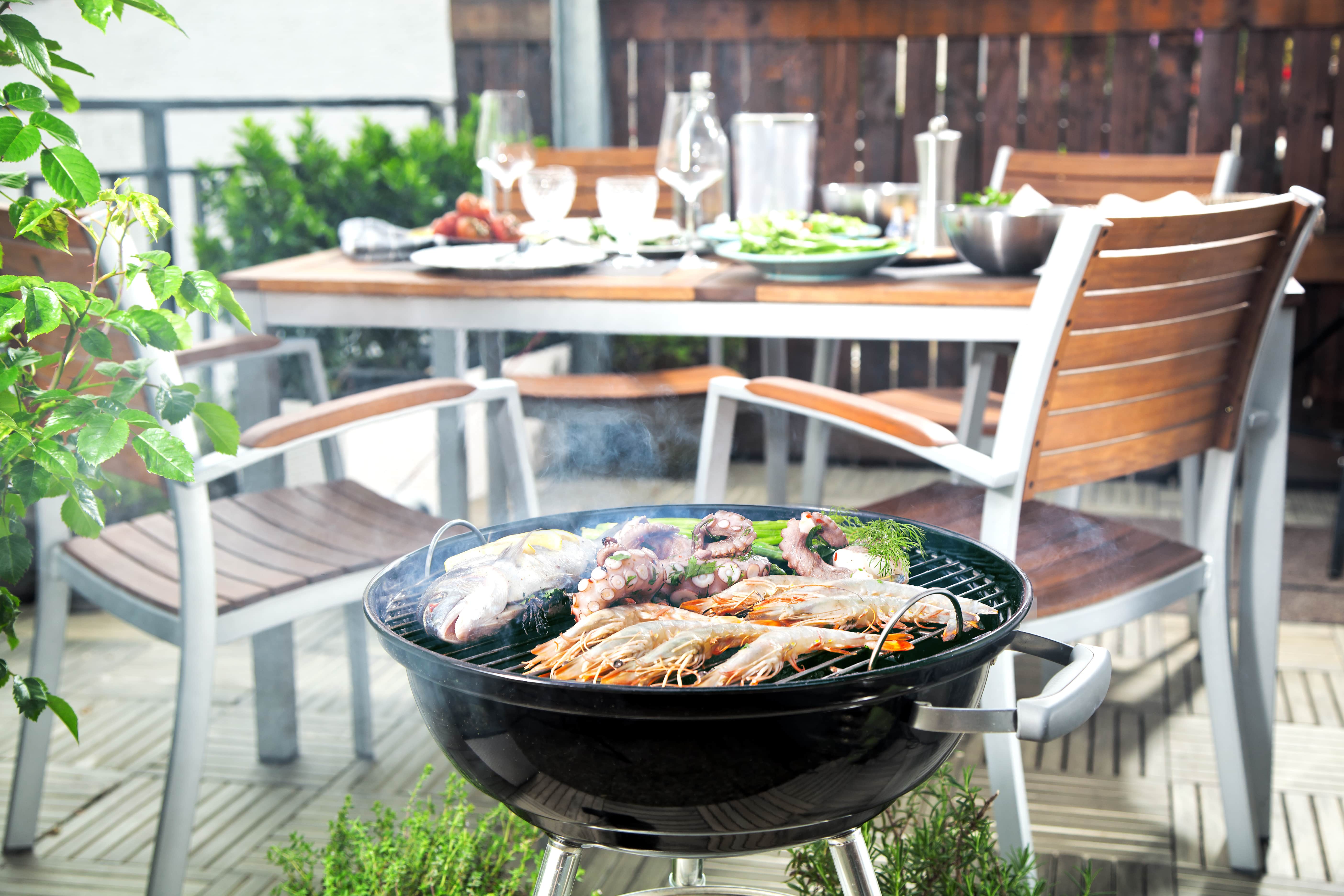 Grill na balkonie, w tle stół z zastawą, rośliny i parawan ogrodowy
