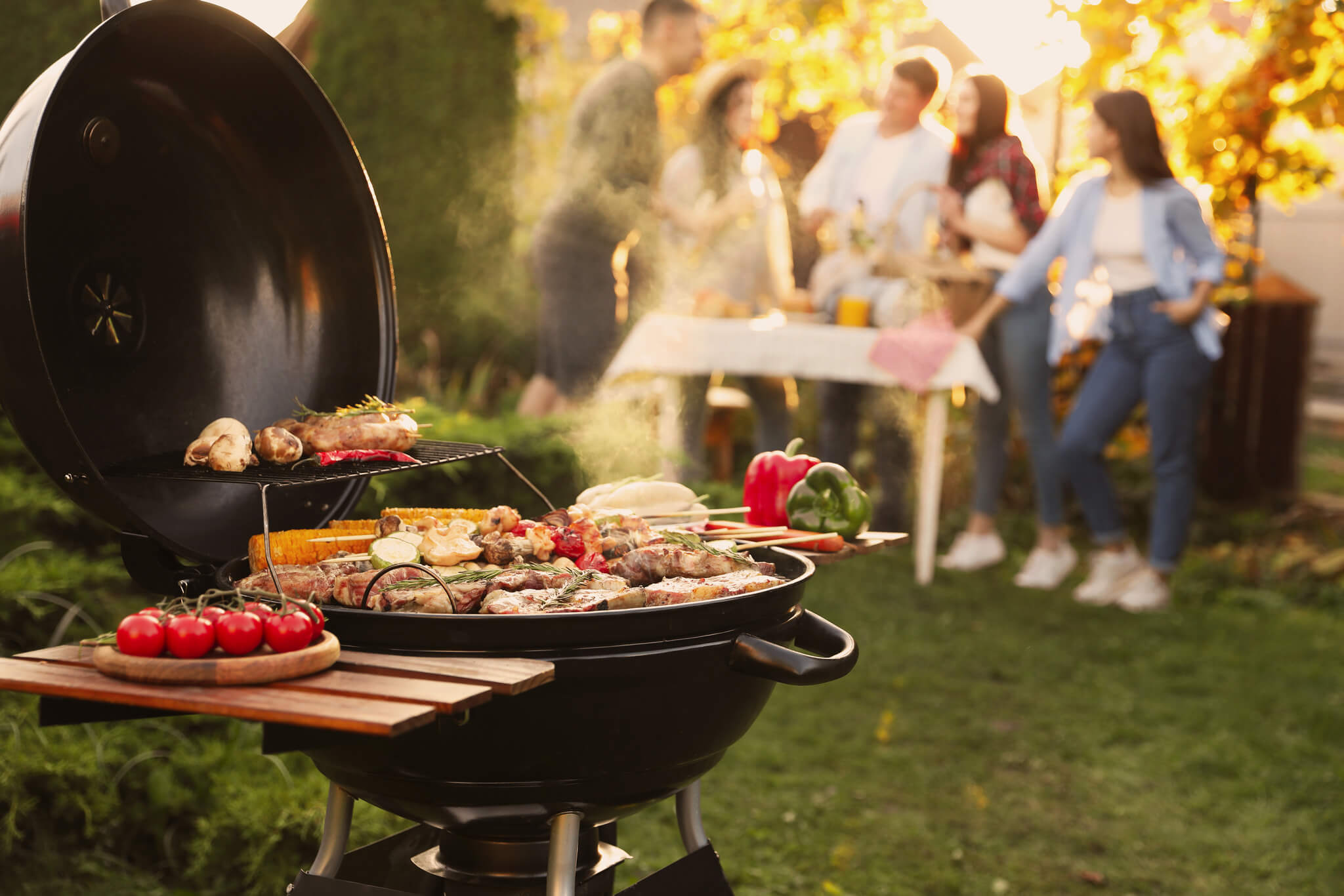 Grill z pokrywą, w tle grupa przyjaciół rozmawia przy stole