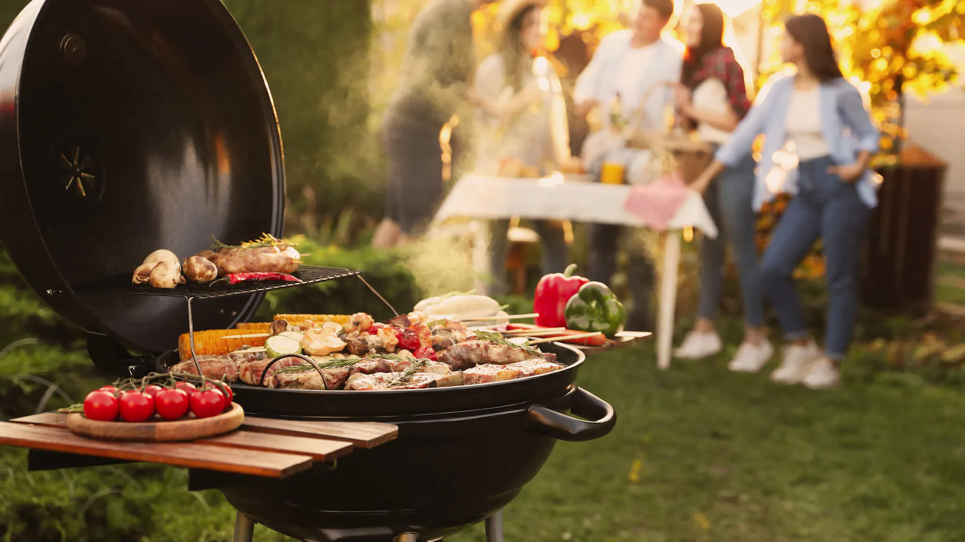 Grill z pokrywą, w tle grupa przyjaciół rozmawia przy stole