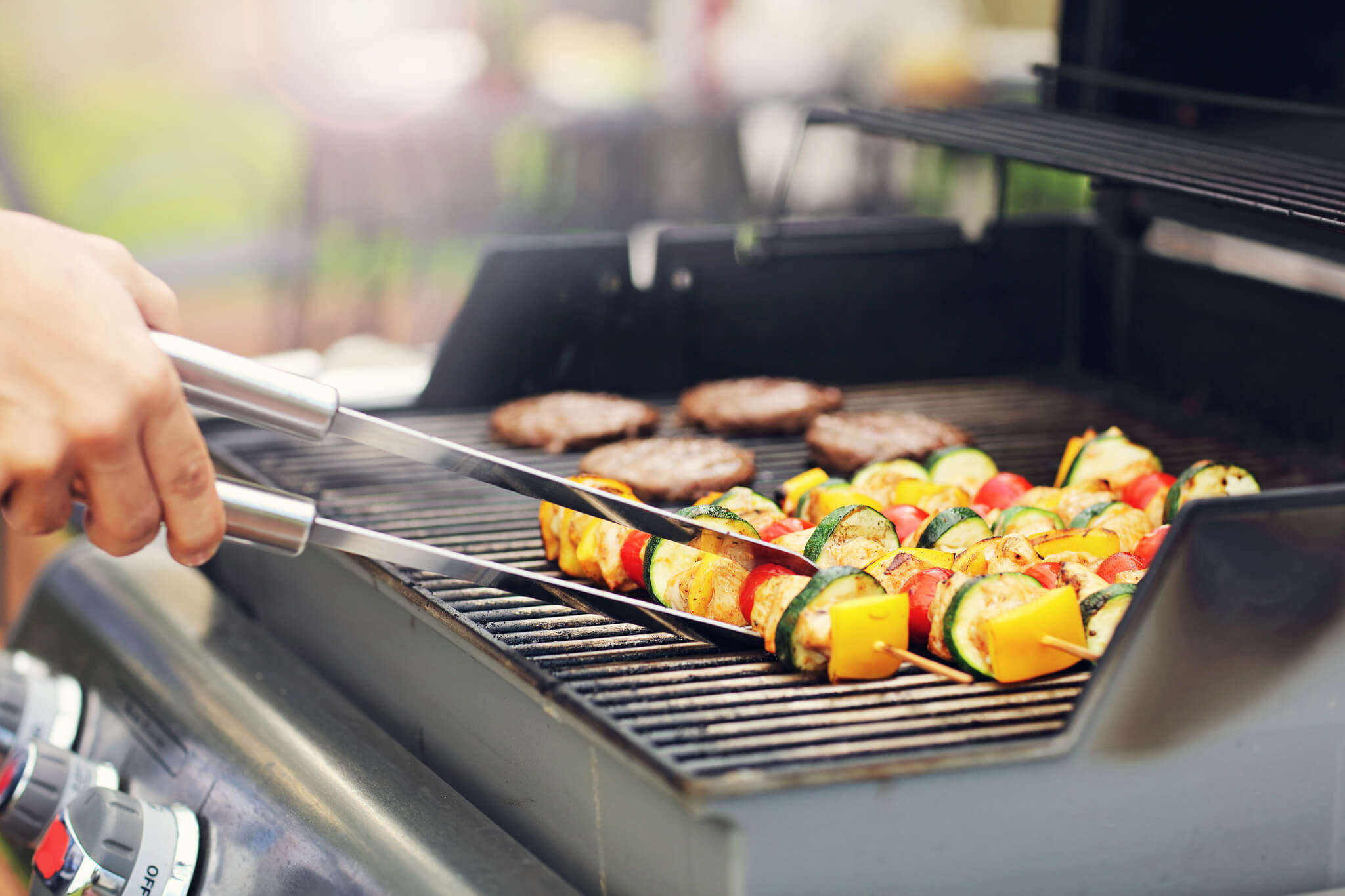 Grill gazowy, a na jego ruszcie znajdują się szaszłyki i mięso