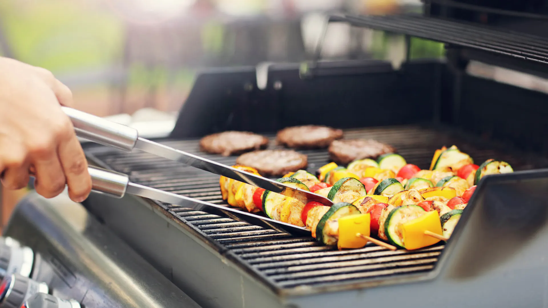 Grill gazowy, a na jego ruszcie znajdują się szaszłyki i mięso