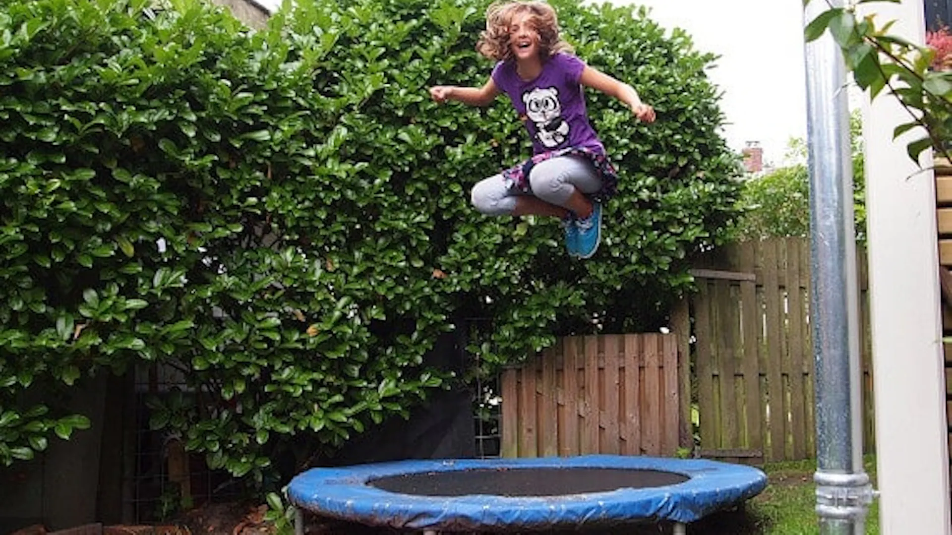 Dziewczynka skacze po niskiej, okrągłej i małej trampolinie w ogrodzie