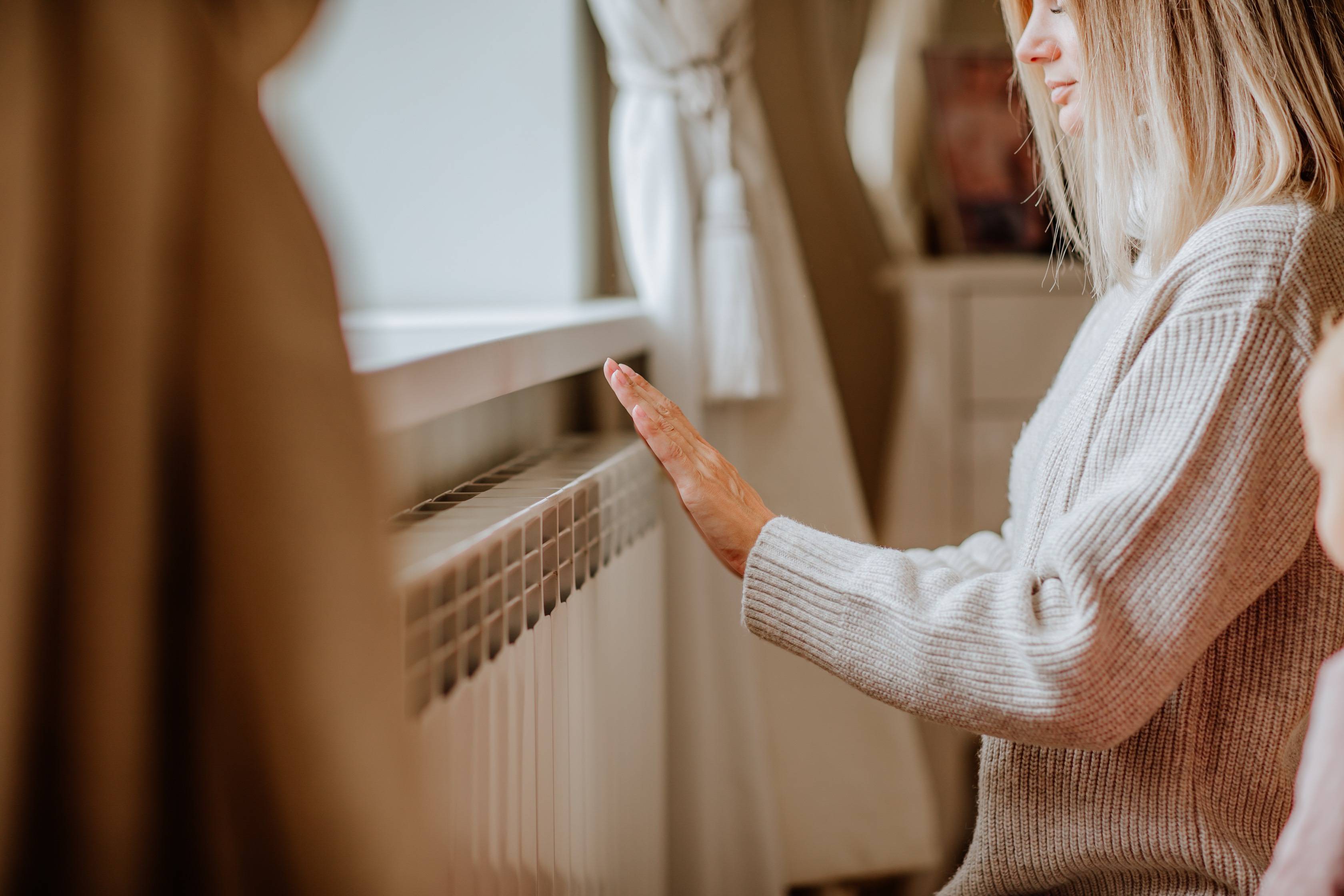 Kobieta ogrzewa się przy grzejniku zasilanym pompą ciepła