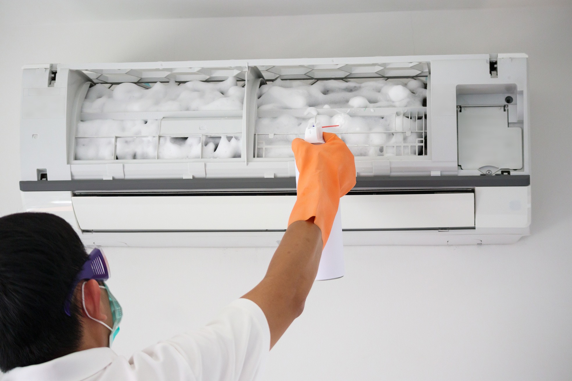 Mężczyzna czyści klimatyzator za pomocą środka chemicznego.