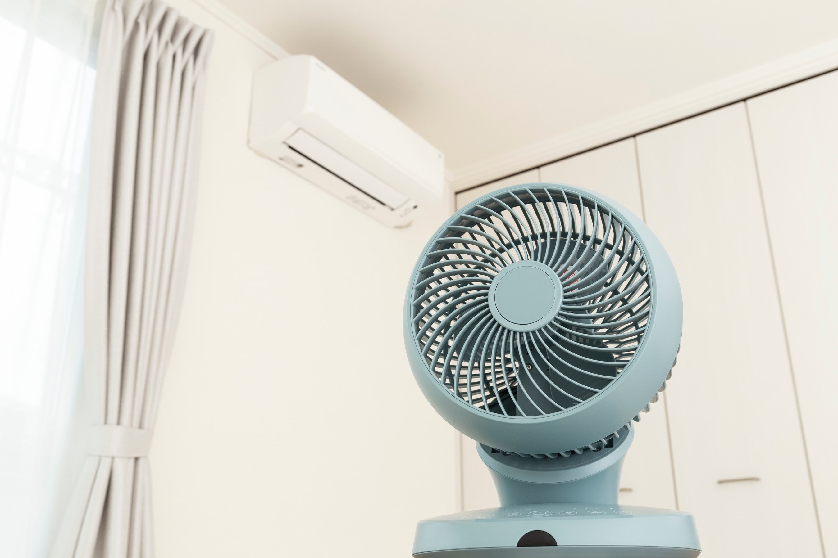 Wentylator biurkowy służy jako ozdoba, w tle na ścianie wisi klimatyzator split