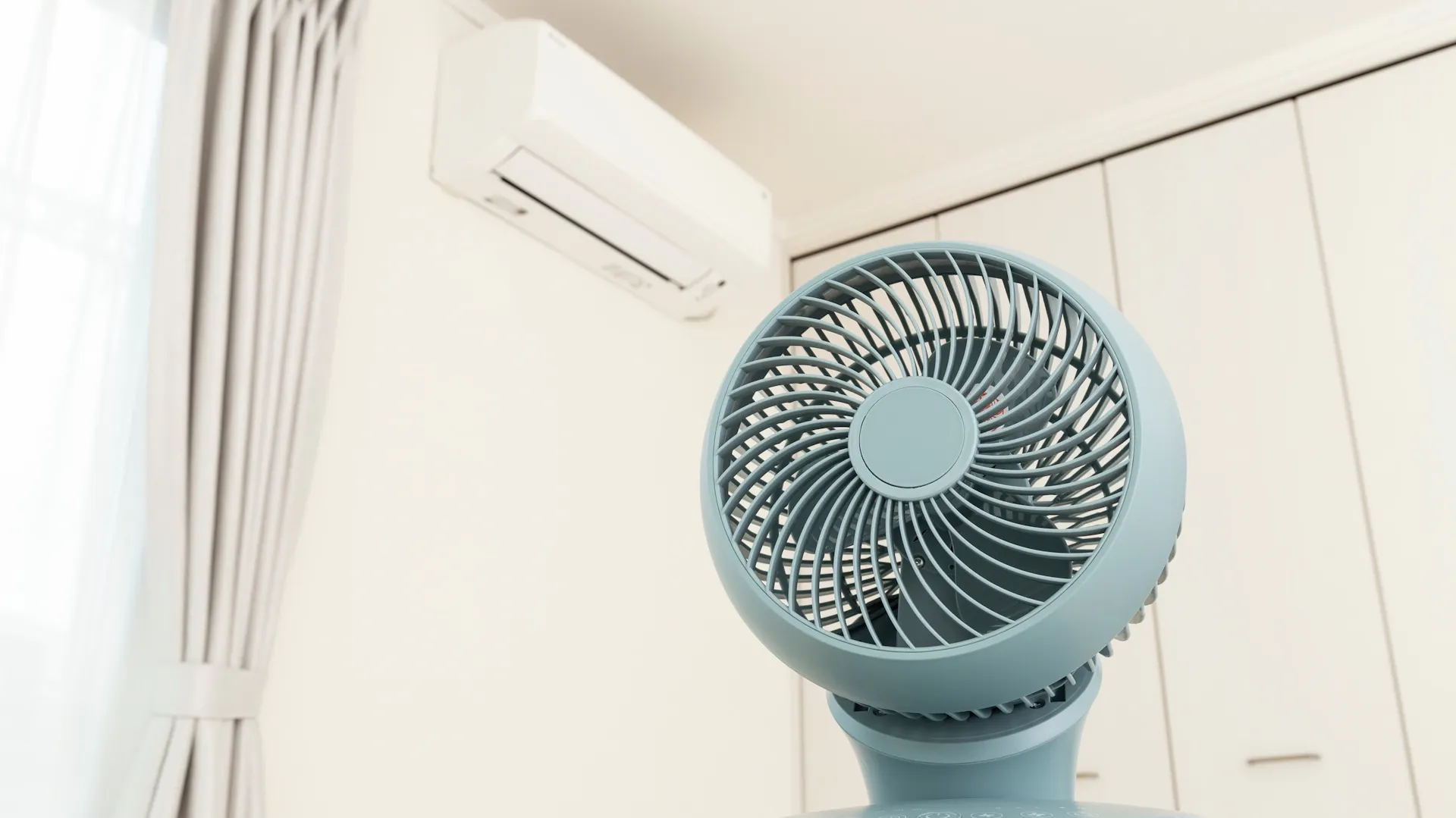 Wentylator biurkowy służy jako ozdoba, w tle na ścianie wisi klimatyzator split