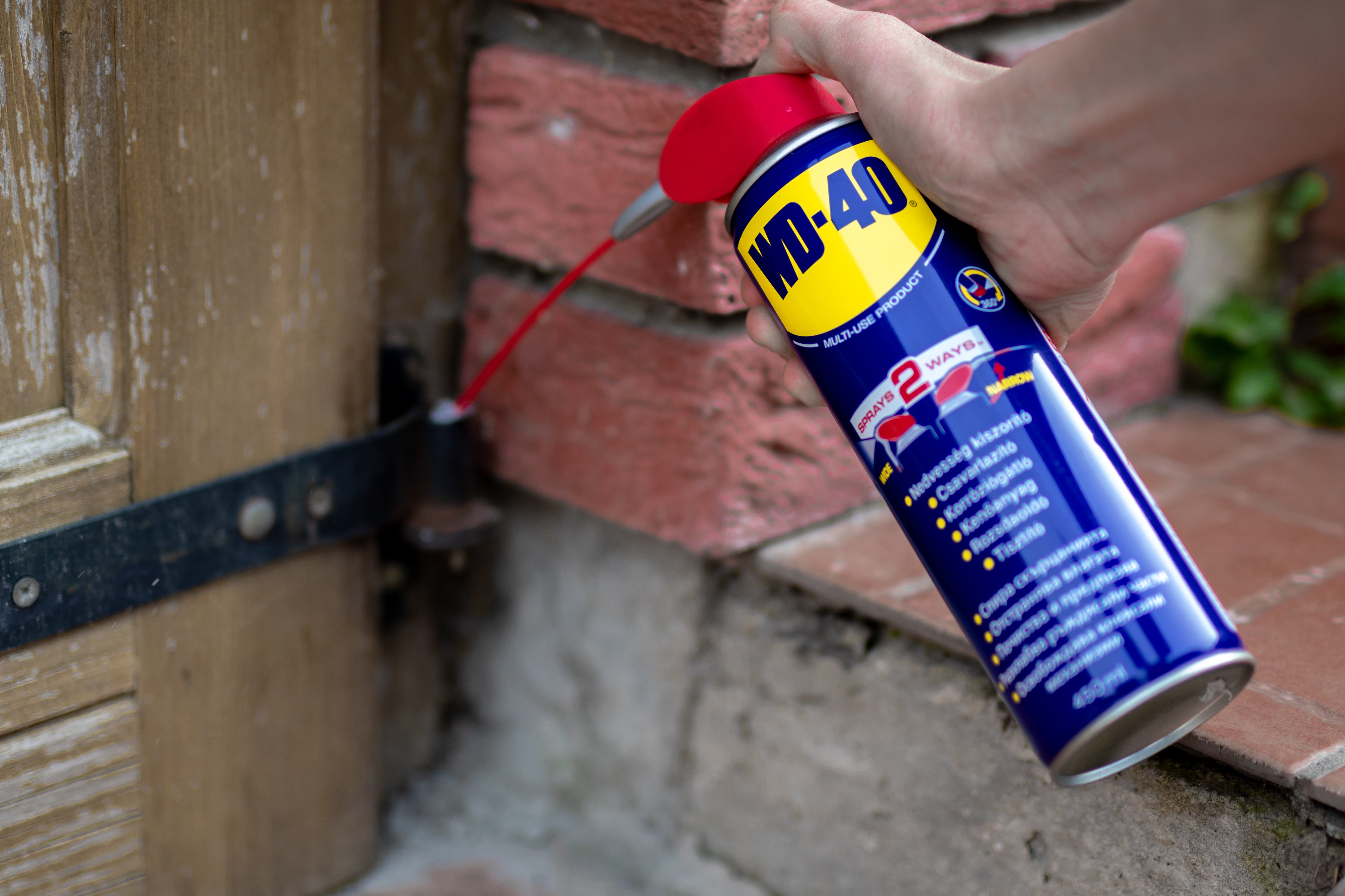 Egy ajtó zsanérjára WD-40-et fújnak.