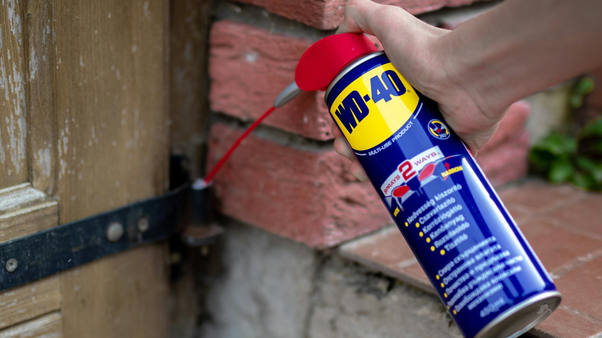 Egy ajtó zsanérjára WD-40-et fújnak.
