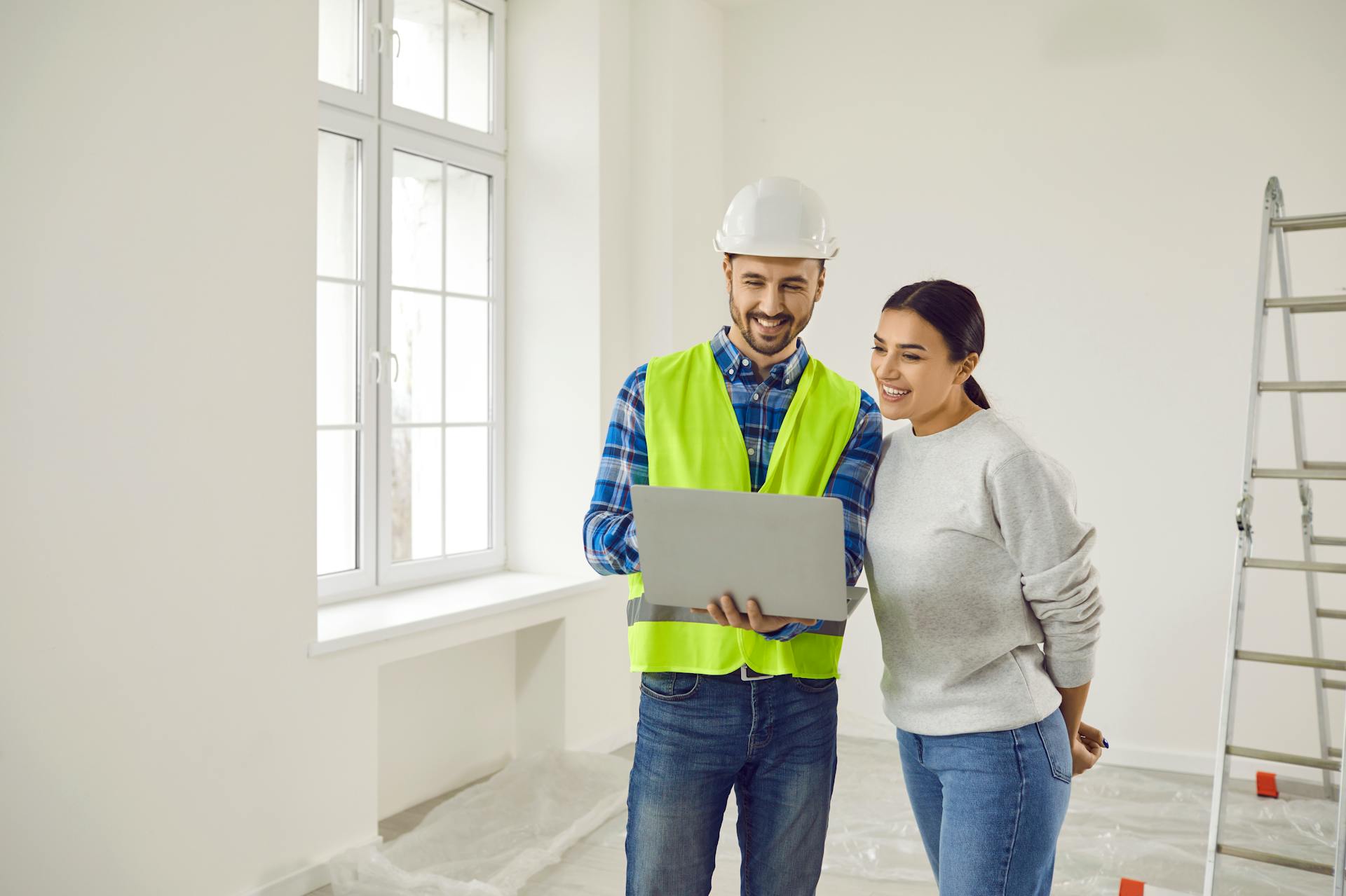 Ein Mann mit Weste und Helm und eine Frau schauen auf ein Tablet in einem renovierten Raum