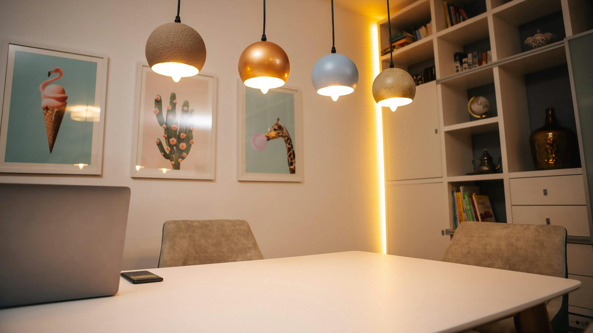 Négyszögletes étkezőasztal egy helyiségben függőlámpákkal az asztal fölött és közvetett megvilágítás a faliszekrényen