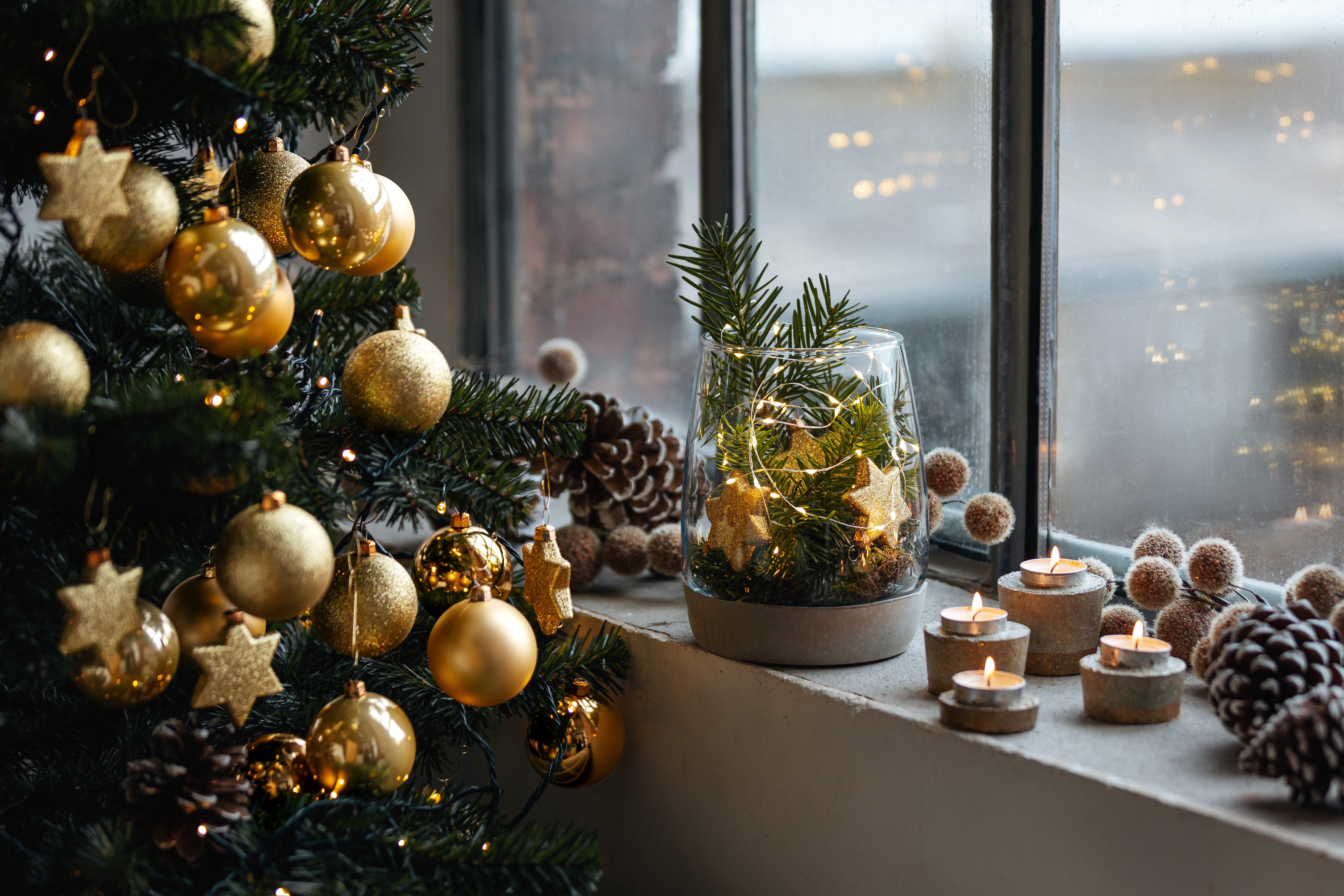 Domácí dekorace se svíčkami vedle zlatem zdobeného vánočního stromku. 