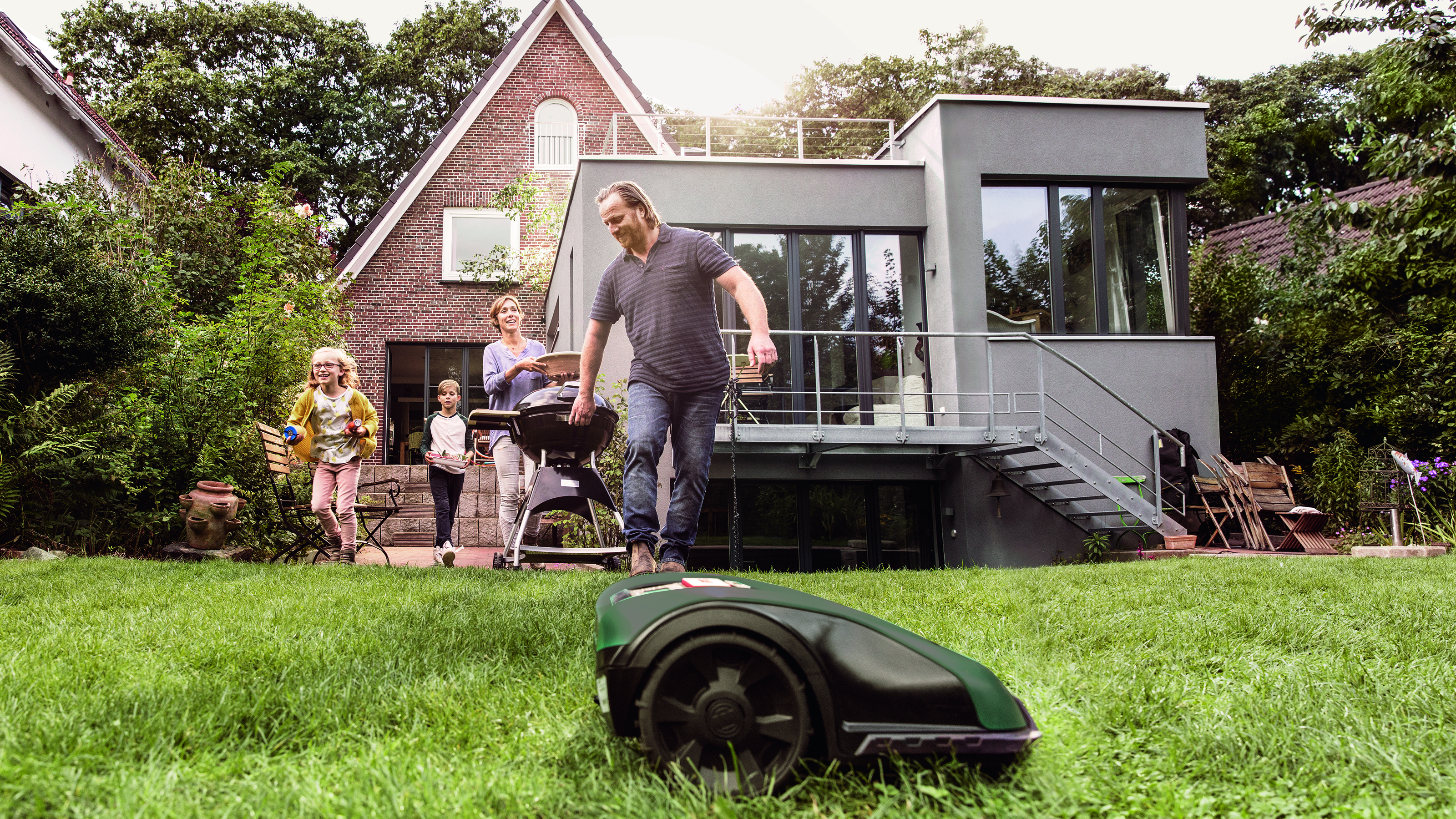 Der Bosch Mähroboter arbeitet, während die Familie die Zeit im Garten genießt.