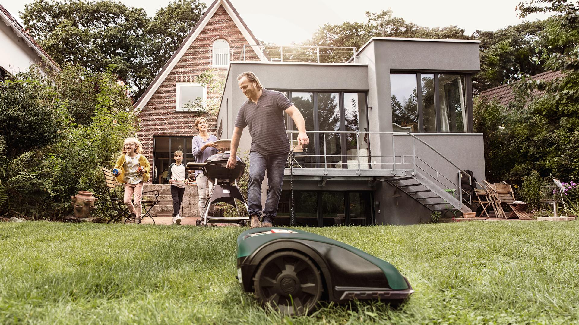 Der Bosch Mähroboter arbeitet, während die Familie die Zeit im Garten genießt.