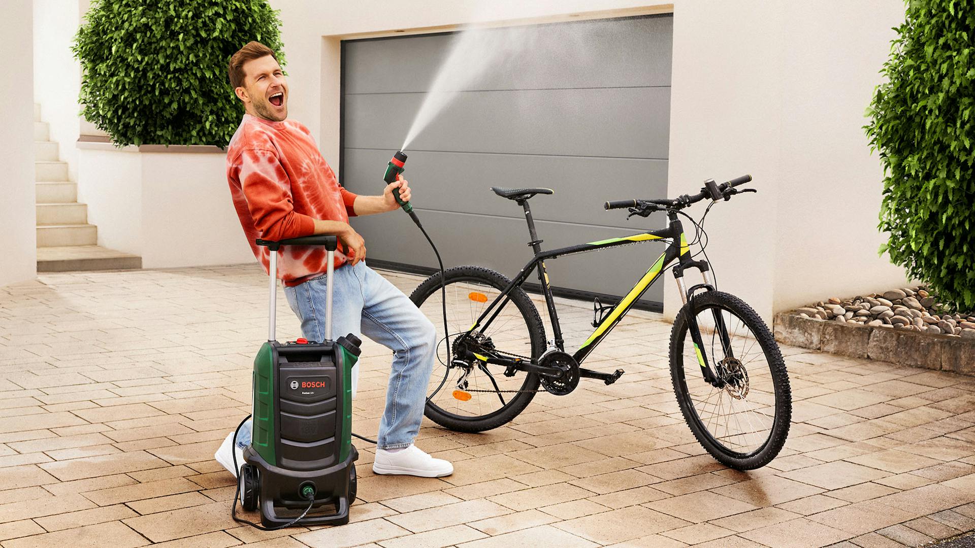 Ein Mann nutzt einen Bosch Hochdruckreiniger, um sein Fahrrad zu reinigen