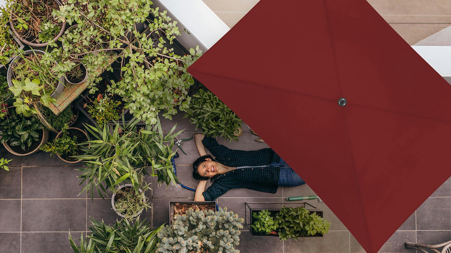 Eine Frau liegt unter einem roten Doppler Sonnenschirm aus der Green Edtion