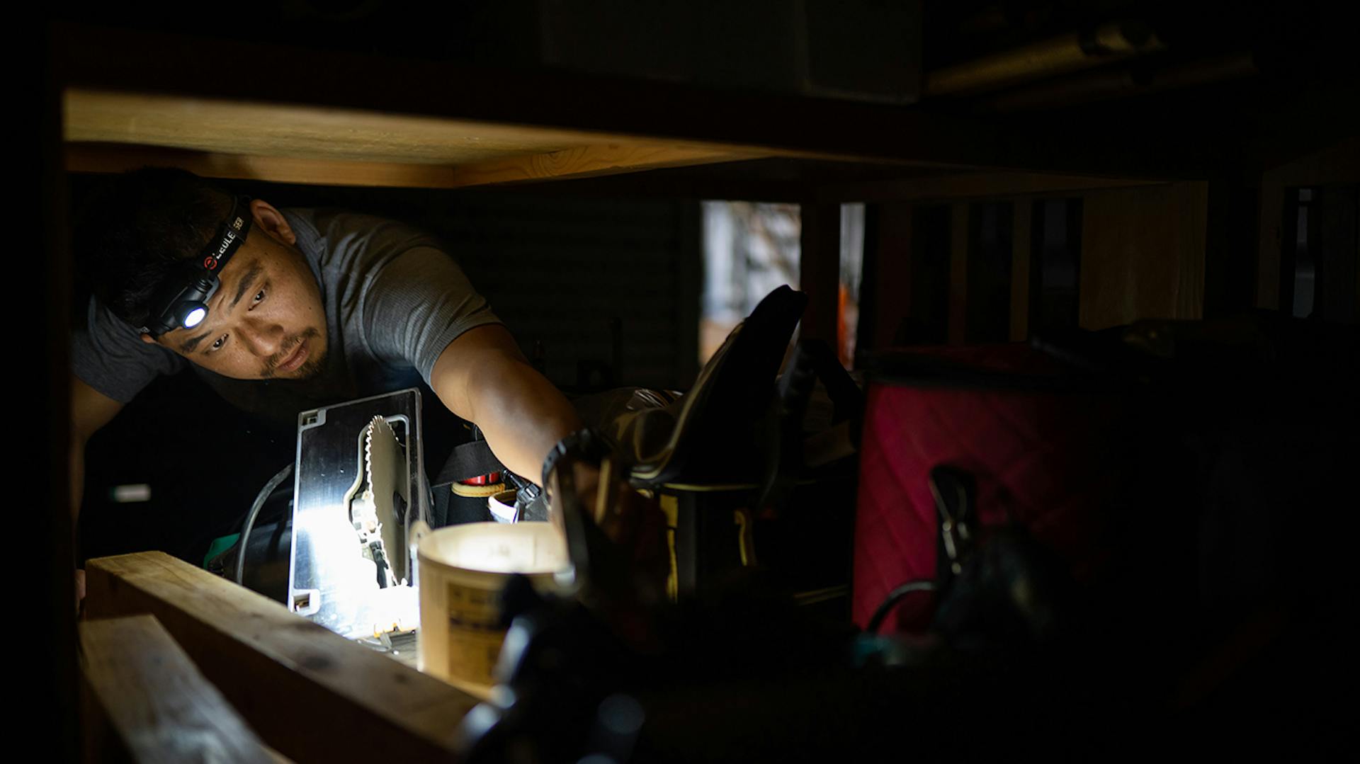 Ein Mann leuchtet mit einer Ledlenser Stirnlampe an eine schwer erreichbare Stelle in der Werkstatt
