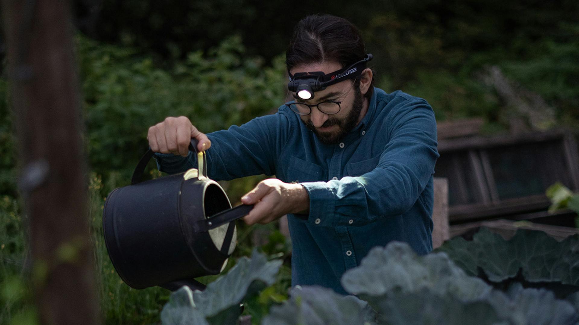 Ein Mann macht Gartenarbeit bei Dämmerung mit Hilfe einer Ledlenser Stirnlampe