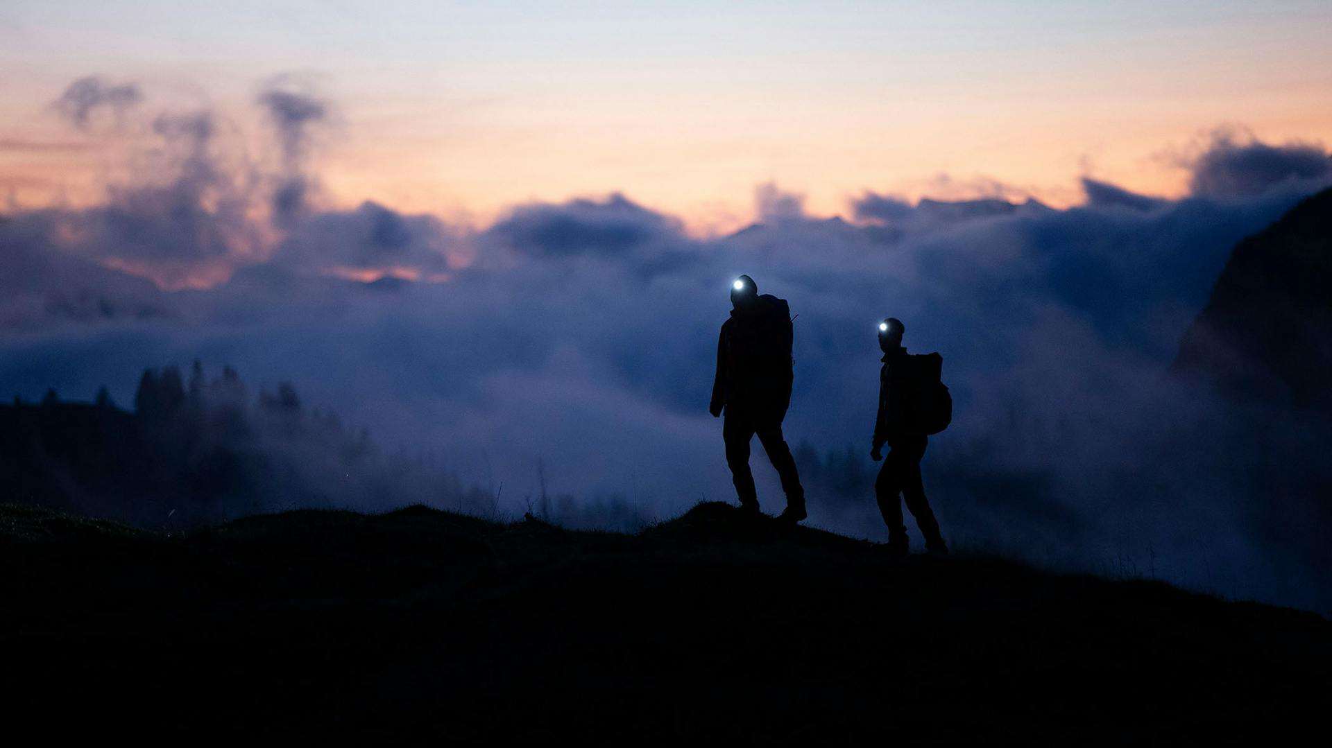 Zwei Personen spazieren in der Dämmerung auf einem Berg mit Ledlenser Stirnlampen
