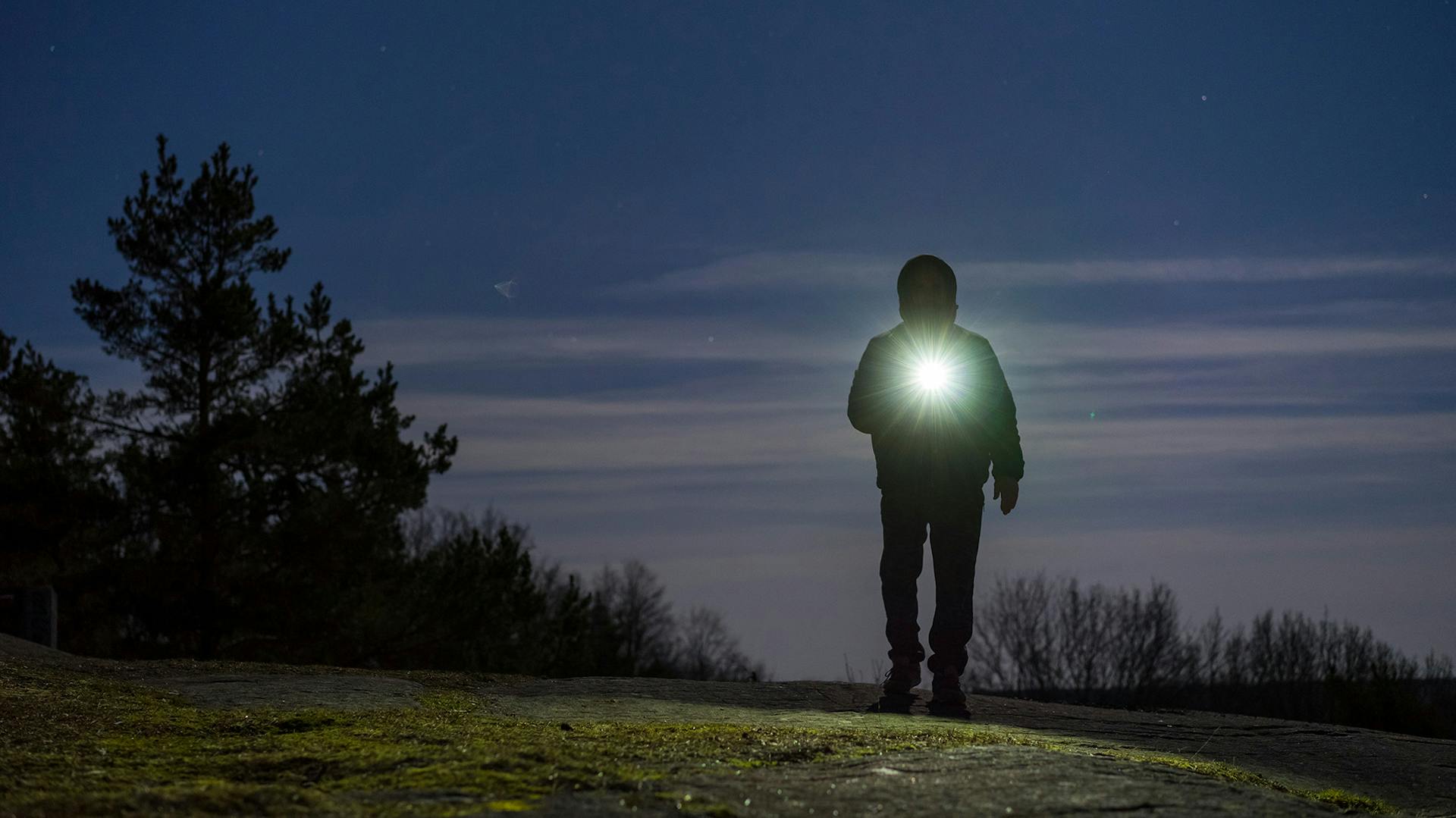 Ein Mann spaziert in der Dämmerung auf einem Hügel mit einer Ledlenser Taschenlampe