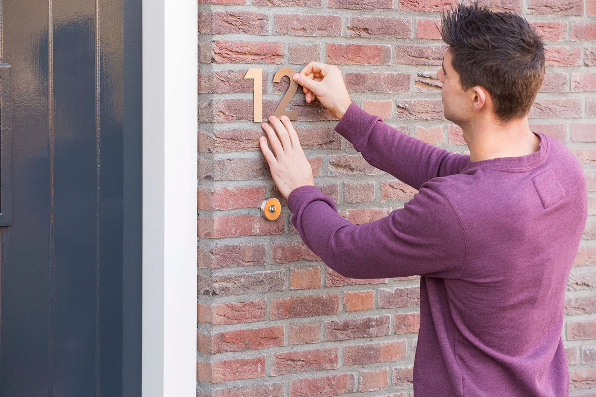Mann nutzt UHU Klebeband zum befestigen der Hausnummer am Haus
