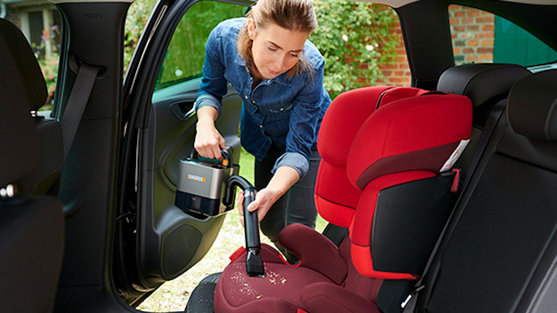 Frau reinigt Auto von innen mit Staubsauger mit Worx Akku