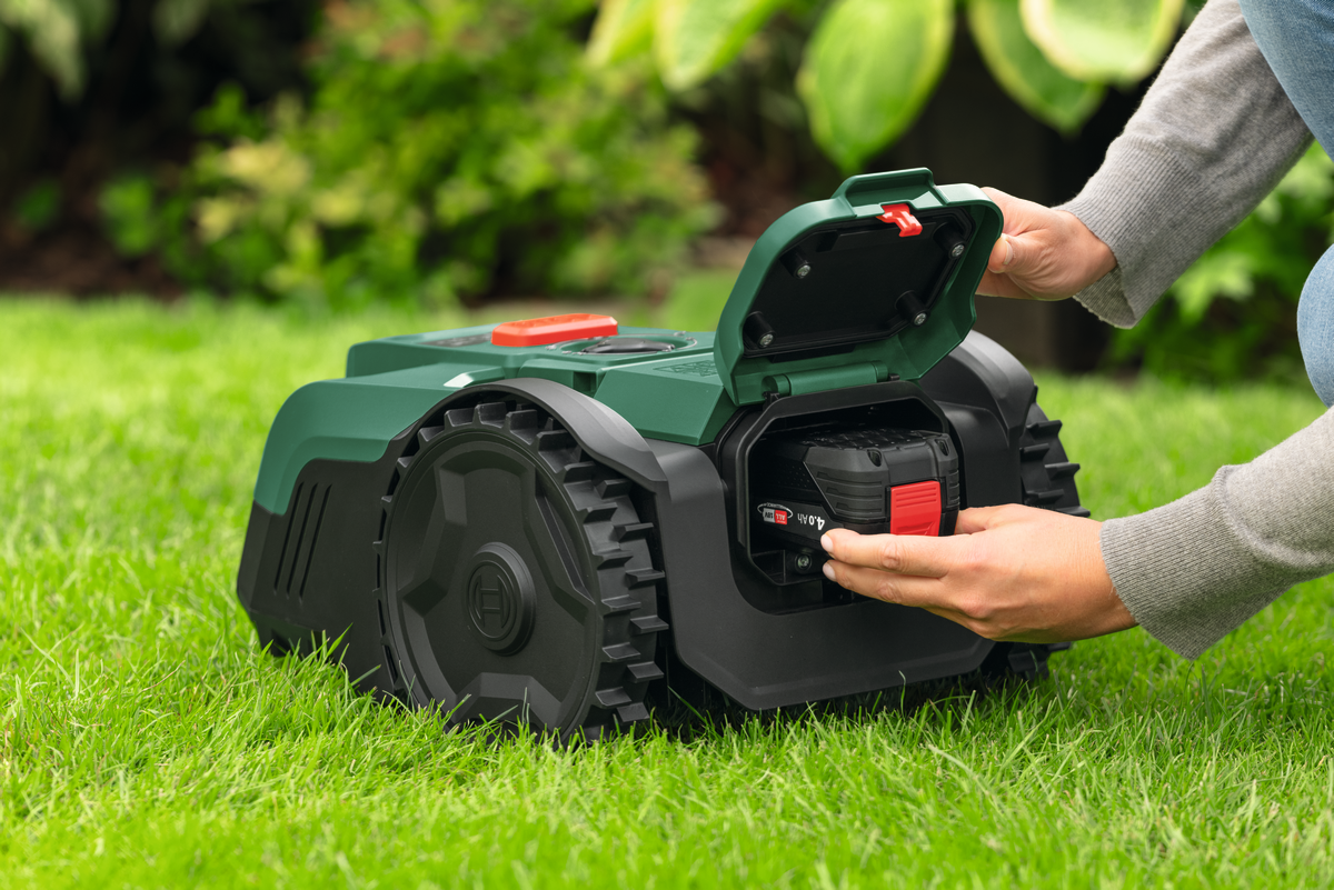 Bosch DIY Mähroboter VISIMOW18V-100 befindet sich auf gründem Rasen und wird von einer Hand angeschlatet.